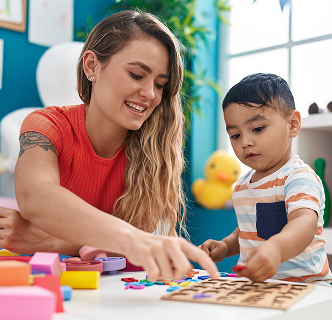 Teacher-toddler-playing-with-maths-puzzle-game-sitting-table-kindergarten 1